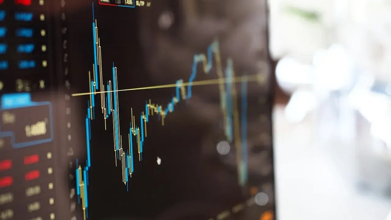 Grafico finanziario su schermo, con candele rosse e blu che indicano fluttuazioni. Potrebbe essere un'istantanea di un trader che effettua operazioni di **insider trading**.