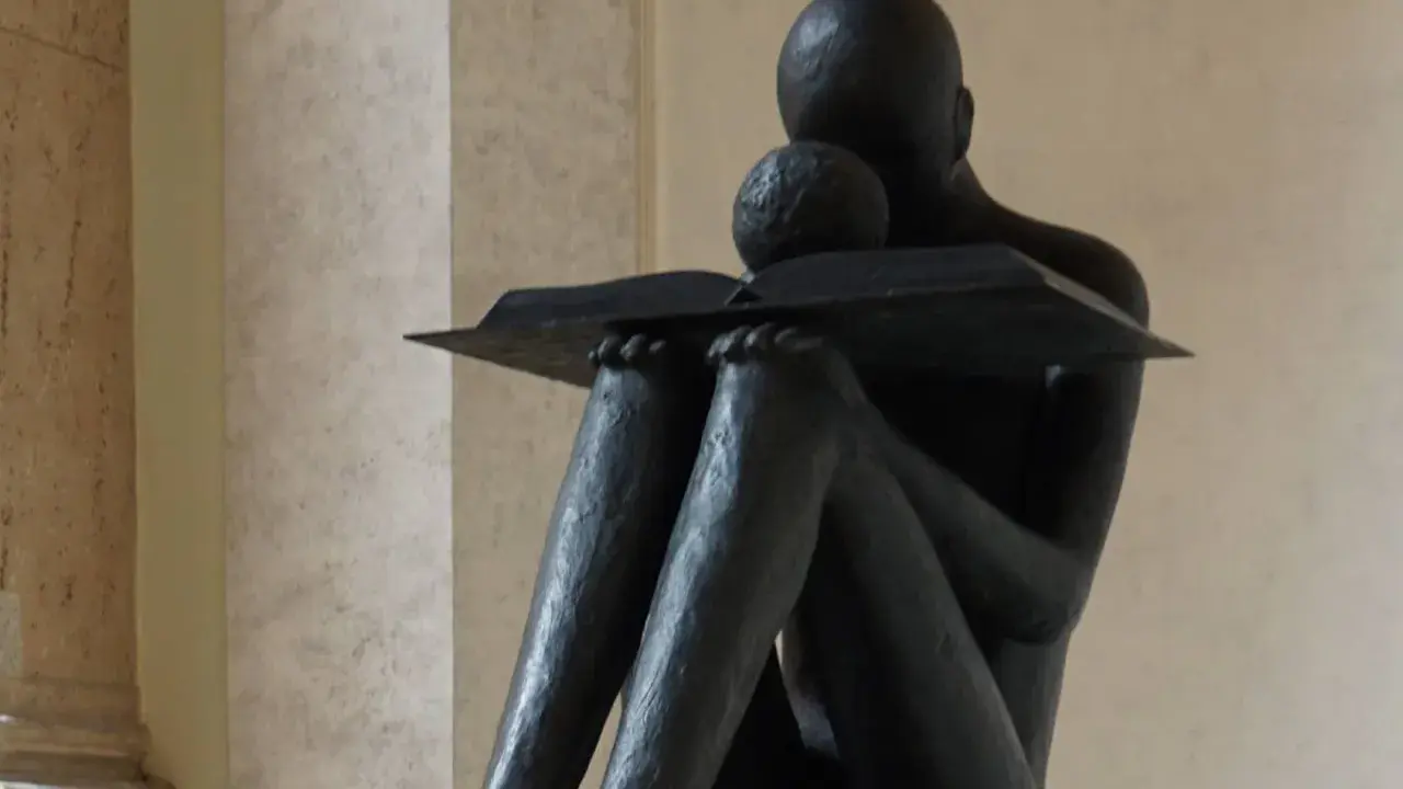 Statua di una figura che legge, con un libro aperto. La scena evoca il profondo significato della conoscenza e della lettura, una vera glossa significato.