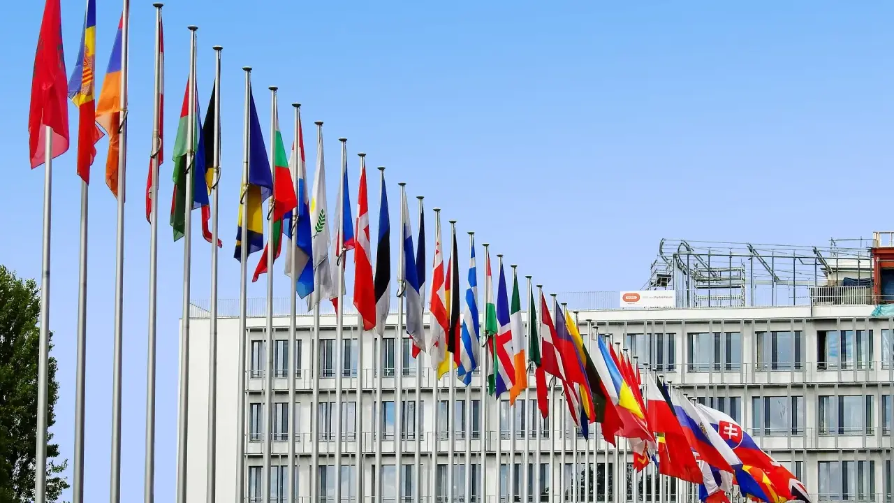 Molte bandiere di stati europei sventolano davanti a un edificio moderno, simbolo di cooperazione e politica internazionale.