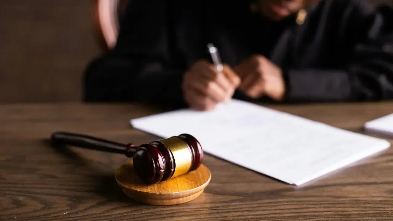 Un giudice scrive documenti legali, con un martelletto da giudice in primo piano. L'incanto significato della giustizia è palpabile.