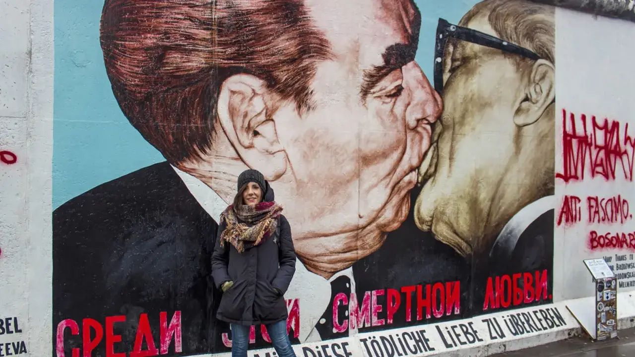 Donna sorride davanti al murale "Il bacio" sull'East Side Gallery, simbolo delle differenze tra Berlino Est e Ovest.