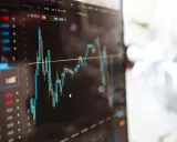 Grafico finanziario su schermo, con candele rosse e blu che indicano fluttuazioni. Potrebbe essere un'istantanea di un trader che effettua operazioni di **insider trading**.