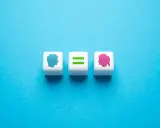 Tre cubi bianchi su sfondo blu. Uno mostra un profilo maschile blu, un altro un segno di uguale verde, e l'ultimo un profilo femminile rosa. Rappresentano l'equità significato.