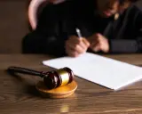 Un giudice scrive documenti legali, con un martelletto da giudice in primo piano. L'incanto significato della giustizia è palpabile.