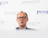 Olaf Scholz, cancelliere tedesco dopo Merkel, parla con espressione seria davanti a uno sfondo con il logo "Presse Club München".