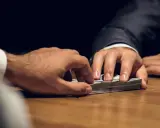 Mani che si scambiano denaro su un tavolo. Un uomo in giacca e cravatta porge una mazzetta di banconote, l'altro le afferra. Il significato di estorsione è chiaro.