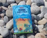 Il libro verde "Verde come l'Italia" giace tra ciottoli levigati, con un'illustrazione di natura e animali.