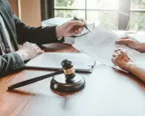 Avvocato e cliente discutono un documento legale, il martelletto del giudice esposto significato di giustizia.