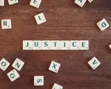 Tessere del gioco compongono la parola "JUSTICE", evocando il suo significato legale e morale.