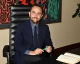 Uomo in giacca blu seduto alla scrivania, con un libro aperto e una penna verde. Un quadro astratto alle sue spalle, che ci fa riflettere su cosa sono le istituzioni.