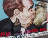 Donna sorride davanti al murale "Il bacio" sull'East Side Gallery, simbolo delle differenze tra Berlino Est e Ovest.