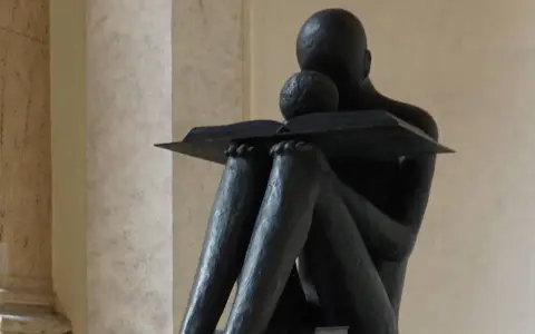 Statua di una figura che legge, con un libro aperto. La scena evoca il profondo significato della conoscenza e della lettura, una vera glossa significato.