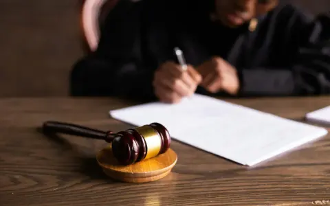 Un giudice scrive documenti legali, con un martelletto da giudice in primo piano. L'incanto significato della giustizia è palpabile.