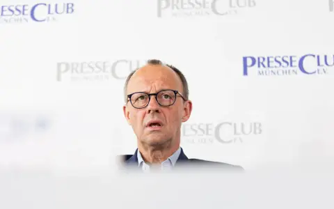 Olaf Scholz, cancelliere tedesco dopo Merkel, parla con espressione seria davanti a uno sfondo con il logo "Presse Club München".