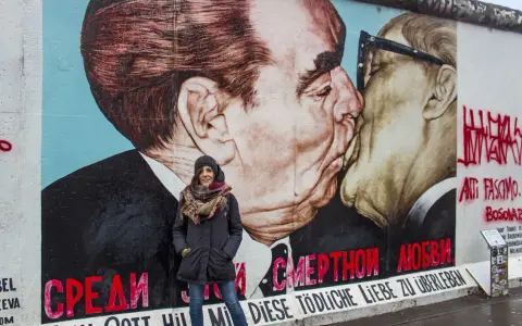 Donna sorride davanti al murale "Il bacio" sull'East Side Gallery, simbolo delle differenze tra Berlino Est e Ovest.