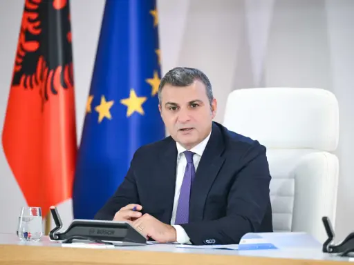 Governatore della **Bank of Albania** in riunione, con le bandiere albanese ed europea sullo sfondo.