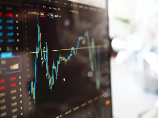 Grafico finanziario su schermo, con candele rosse e blu che indicano fluttuazioni. Potrebbe essere un'istantanea di un trader che effettua operazioni di **insider trading**.