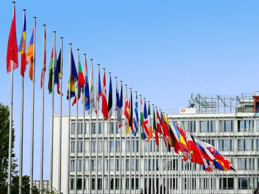 Molte bandiere di stati europei sventolano davanti a un edificio moderno, simbolo di cooperazione e politica internazionale.