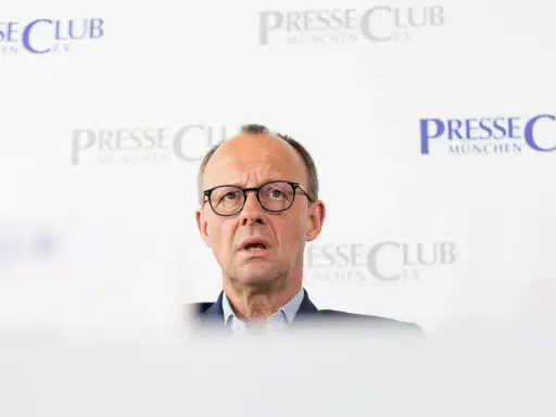 Olaf Scholz, cancelliere tedesco dopo Merkel, parla con espressione seria davanti a uno sfondo con il logo "Presse Club München".