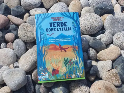 Il libro verde "Verde come l'Italia" giace tra ciottoli levigati, con un'illustrazione di natura e animali.