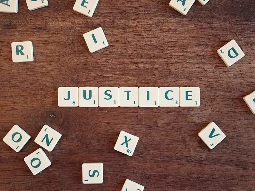 Tessere del gioco compongono la parola "JUSTICE", evocando il suo significato legale e morale.