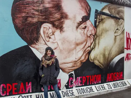 Donna sorride davanti al murale "Il bacio" sull'East Side Gallery, simbolo delle differenze tra Berlino Est e Ovest.