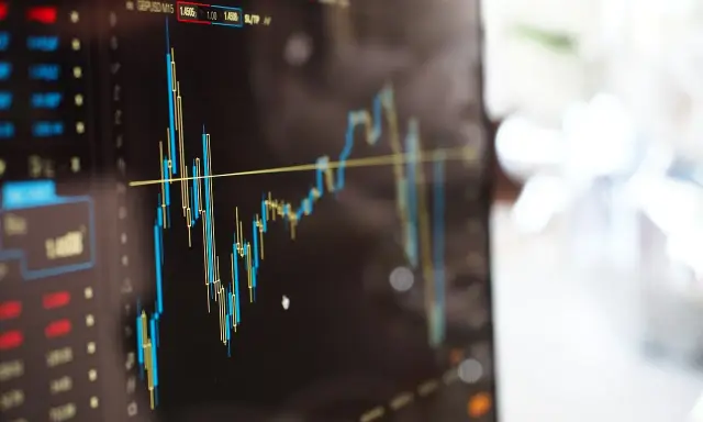 Grafico finanziario su schermo, con candele rosse e blu che indicano fluttuazioni. Potrebbe essere un'istantanea di un trader che effettua operazioni di **insider trading**.