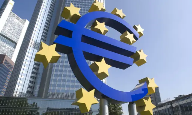 Simbolo dell'Euro con stelle gialle davanti a grattacieli moderni, evocando la stabilità della politica fiscale europea.
