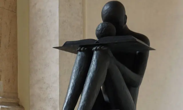 Statua di una figura che legge, con un libro aperto. La scena evoca il profondo significato della conoscenza e della lettura, una vera glossa significato.