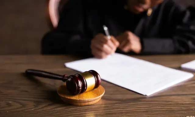 Un giudice scrive documenti legali, con un martelletto da giudice in primo piano. L'incanto significato della giustizia è palpabile.