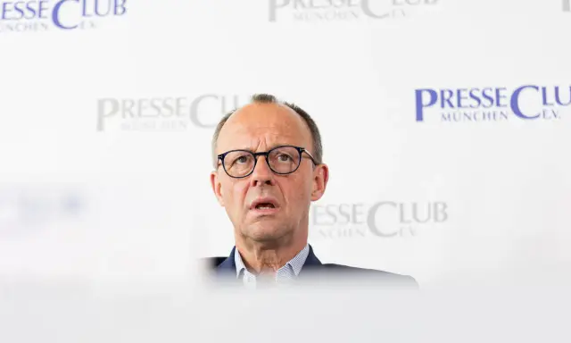 Olaf Scholz, cancelliere tedesco dopo Merkel, parla con espressione seria davanti a uno sfondo con il logo "Presse Club München".