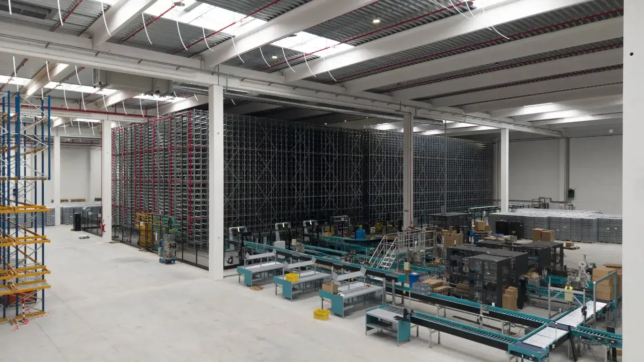 Magazzino automatizzato con scaffalature alte, nastri trasportatori e macchinari per la logistica, esempio di economia di scala.