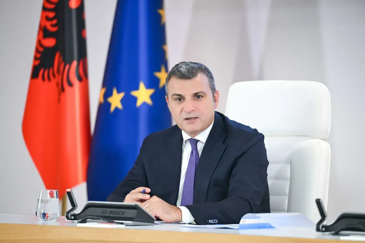 Uomo in giacca e cravatta, con bandiera albanese e UE. Potrebbe essere un rappresentante della Bank of Albania.