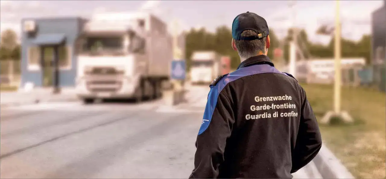 Guardia di confine sorveglia un camion in transito, pronto a verificare la merce e la corretta applicazione della tariffa doganale.