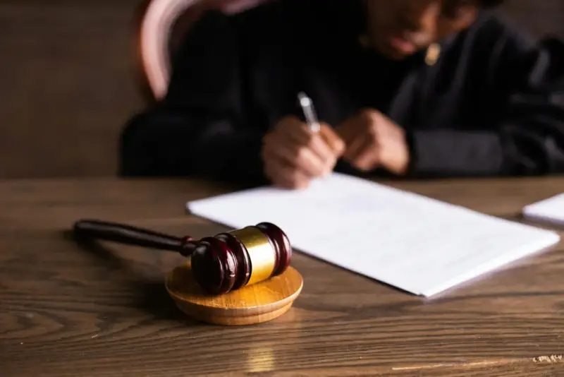 Un giudice scrive documenti legali, con un martelletto da giudice in primo piano. L'incanto significato della giustizia è palpabile.